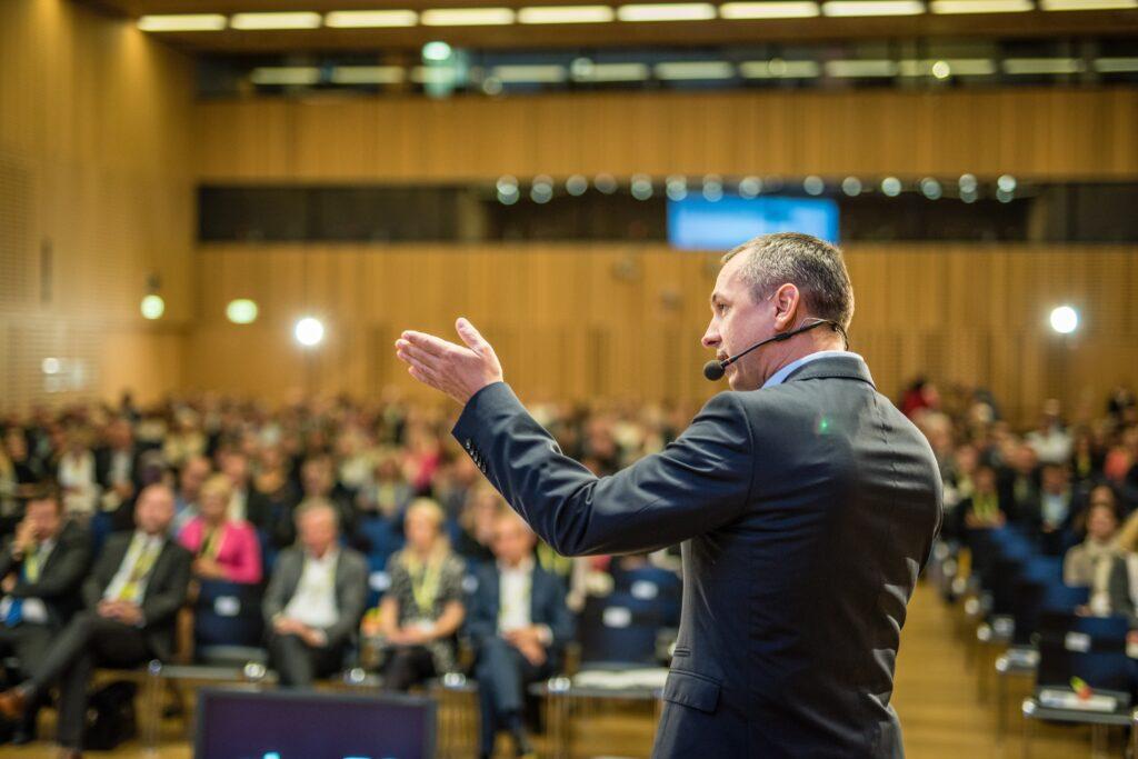 Relatore su palco in auditorium durante evento, esempio di progettazione auditorium e soluzioni sale congressi per conferenze e meeting aziendali.