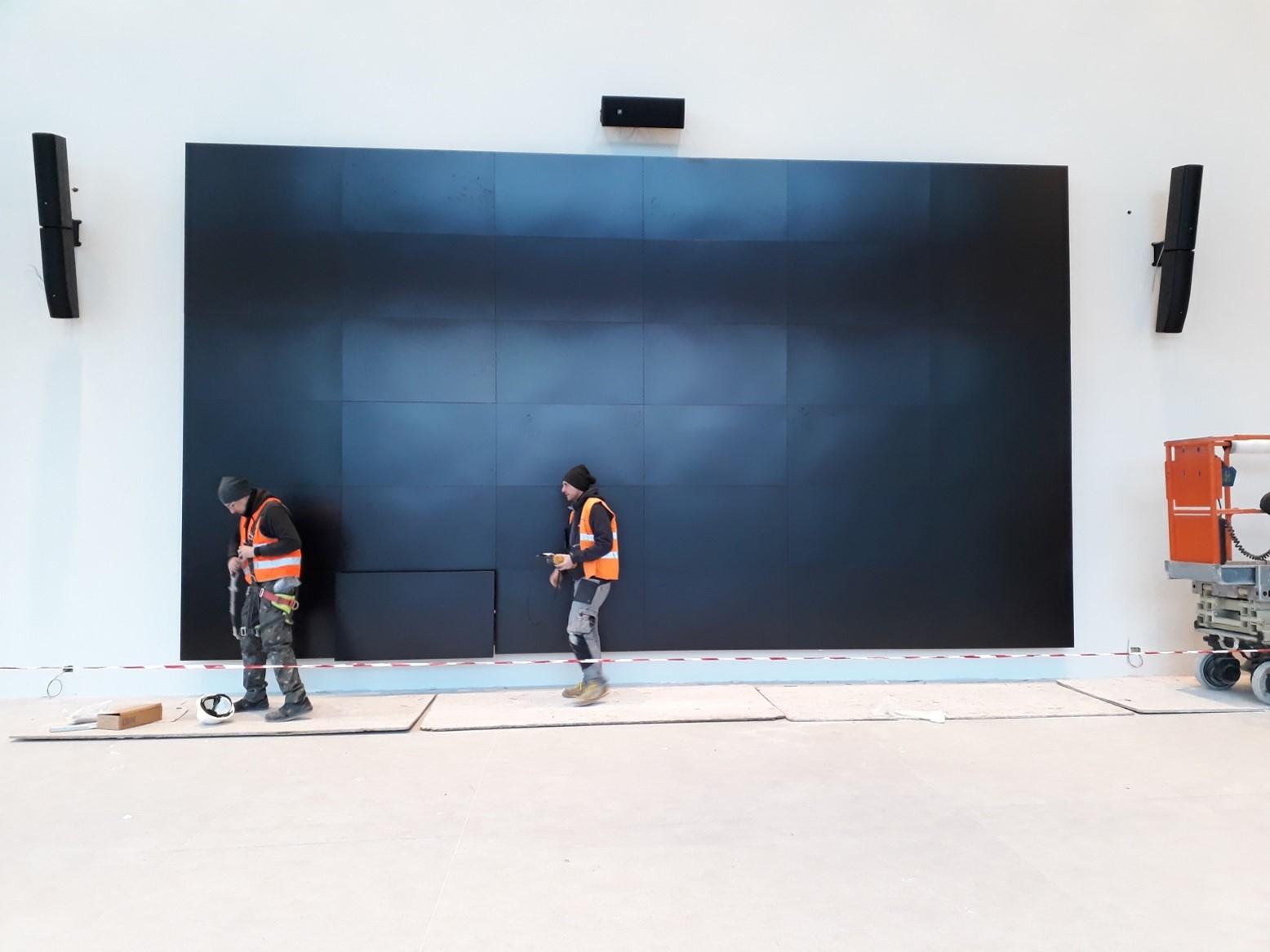 Tecnici al lavoro su grande display durante integrazione audio video e installazione audio video in ambiente professionale.