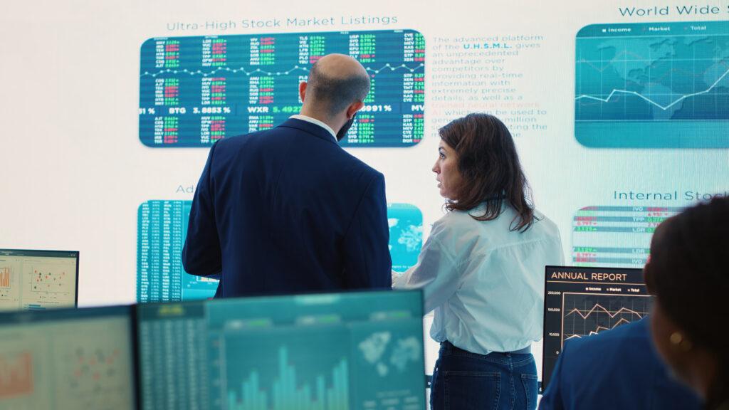 Sala di controllo audio video con videowall informativo e operatori che monitorano dati e report in tempo reale.