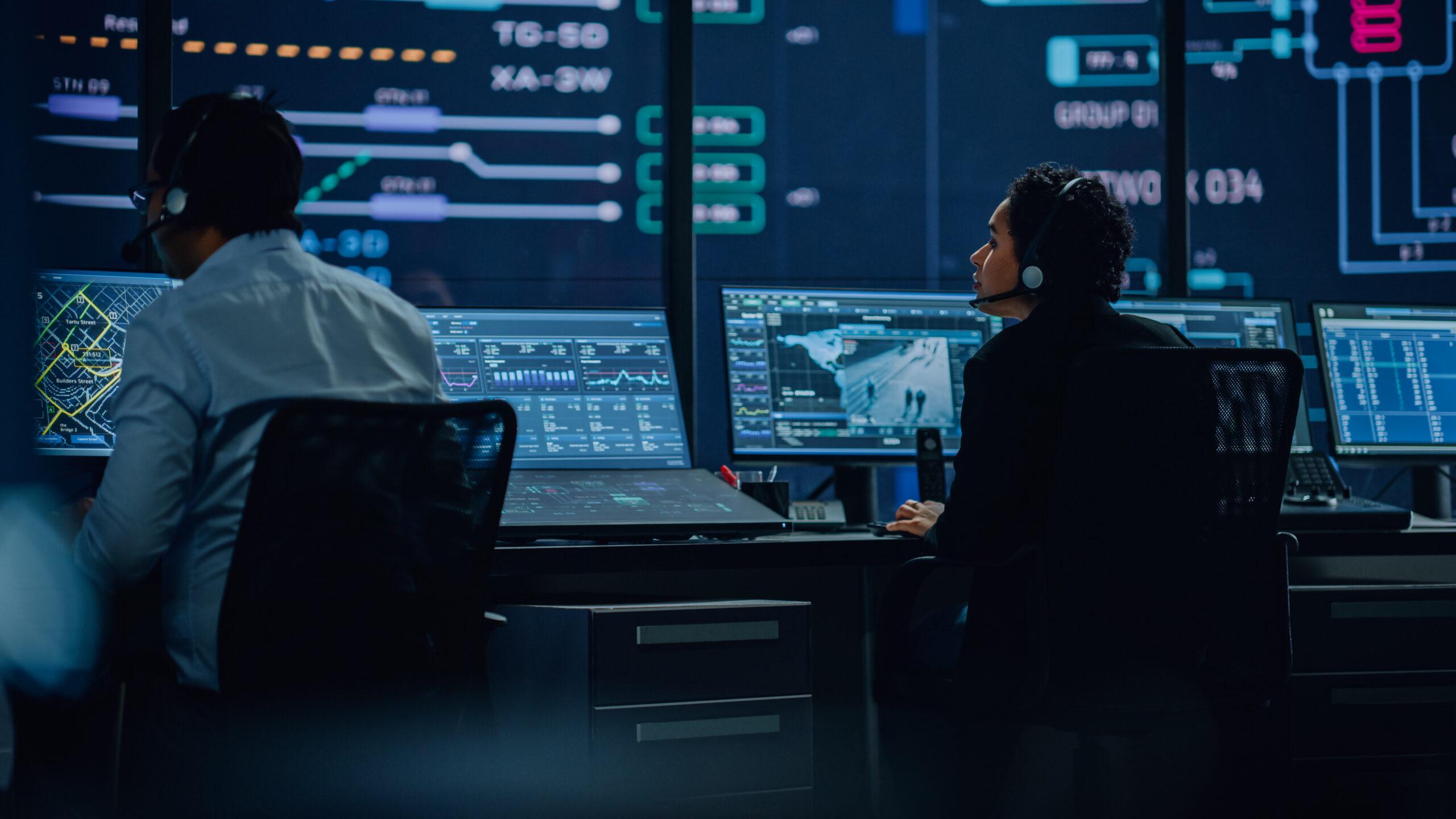 Operatori al lavoro in sala di controllo con monitor multipli, esempio di sala sorveglianza per gestione sicurezza e supervisione impianti.