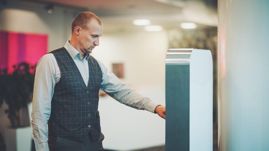 Uomo utilizza un totem multimediale interattivo in ambiente aziendale per comunicazione digital signage.