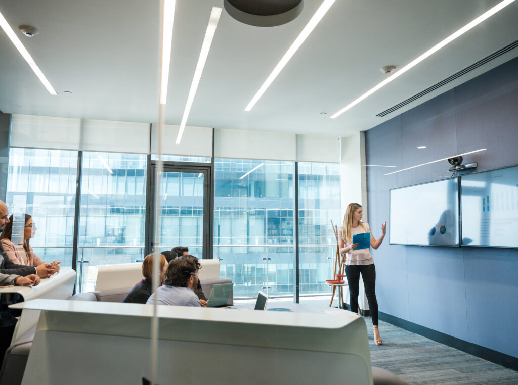 Audio video professionale in sala riunione moderna con sistema di videoconferenza, presentazione su display e partecipanti in meeting per lavoro ibrido.