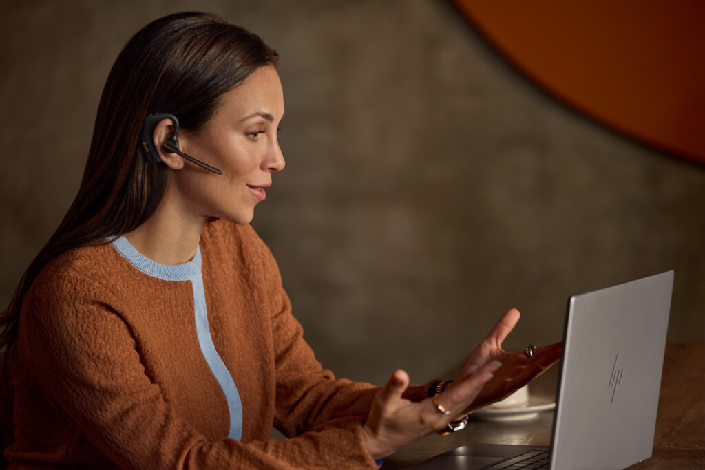 Donna in videocall con cuffie professionali e laptop, esempio di cuffie business per lavoro da remoto e comunicazione aziendale.
