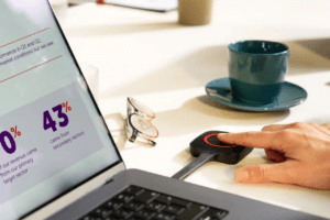 Mano che utilizza un dispositivo Barco Clickshare per avviare una videoconferenza su laptop con slide di dati.