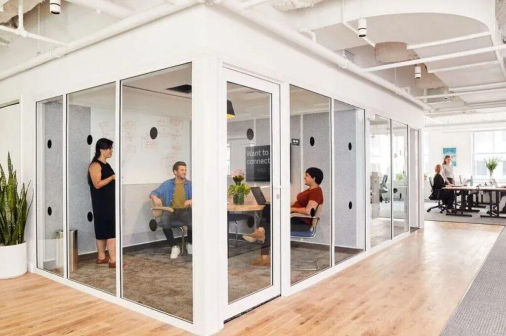 Huddle room in ufficio moderno con pareti in vetro, utilizzata come sala riunione per videoconferenza e collaborazione tra team.