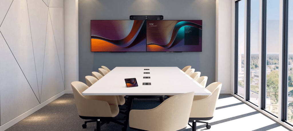Sala riunioni moderna con tavolo centrale e sedute, parete decorata con grafica geometrica colorata, configurata come Microsoft Teams Room (MTR) per videoconferenza.