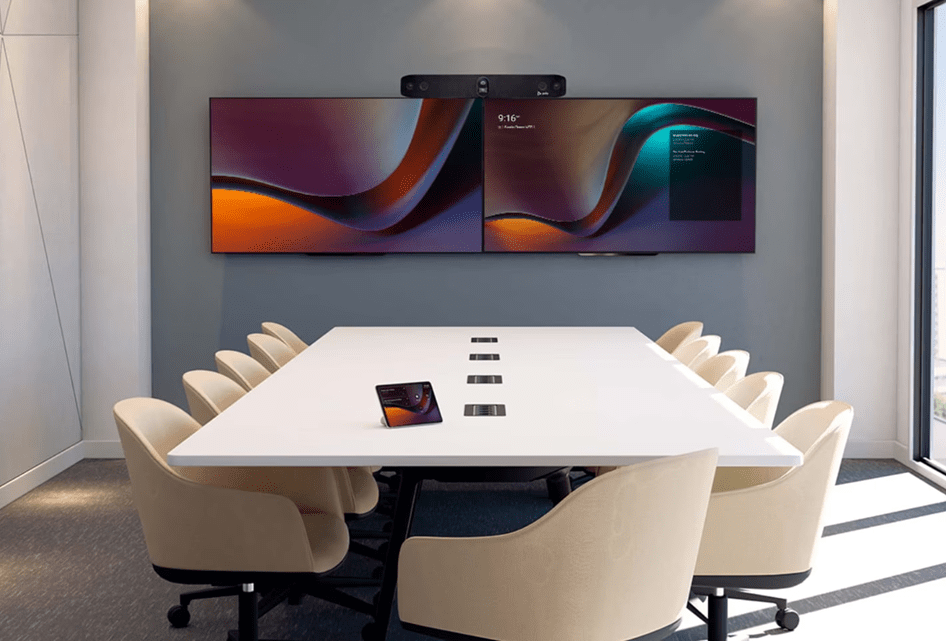 Sala riunioni moderna con tavolo centrale e sedute, parete decorata con grafica geometrica colorata, configurata come Microsoft Teams Room (MTR) per videoconferenza.